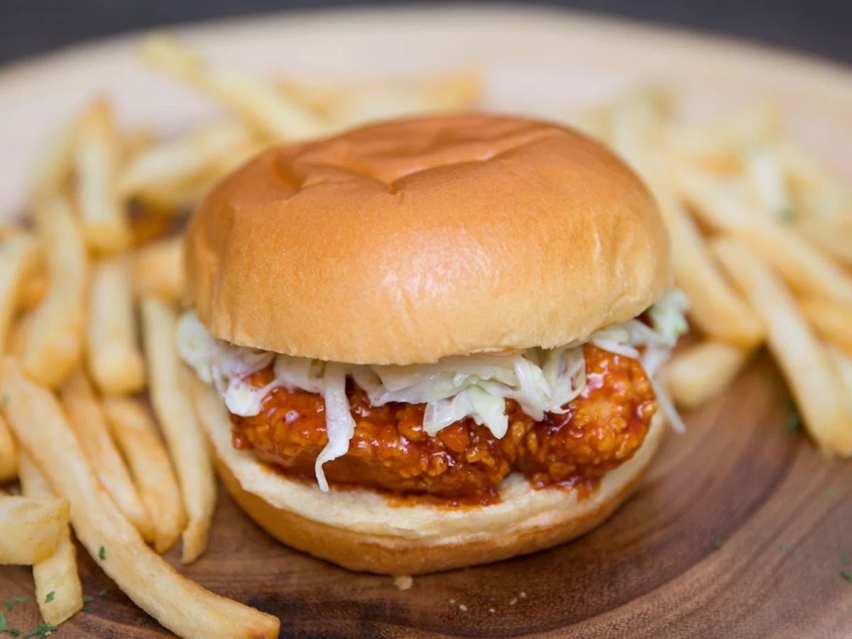 Fried chicken sandwich with red-sauced chicken and coleslaw beside french fries