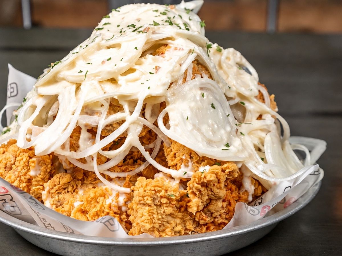 Crispy fried chicken buried under thin-sliced white onion rings in a creamy white sauce with parsley flakes