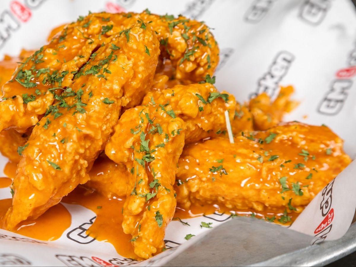 Fried chicken tenders coated in a bright orange creamy sauce with parsley flakes